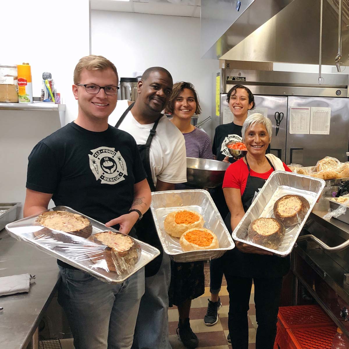 A small group of staff and volunteers in an industrial kitchen with prepared food