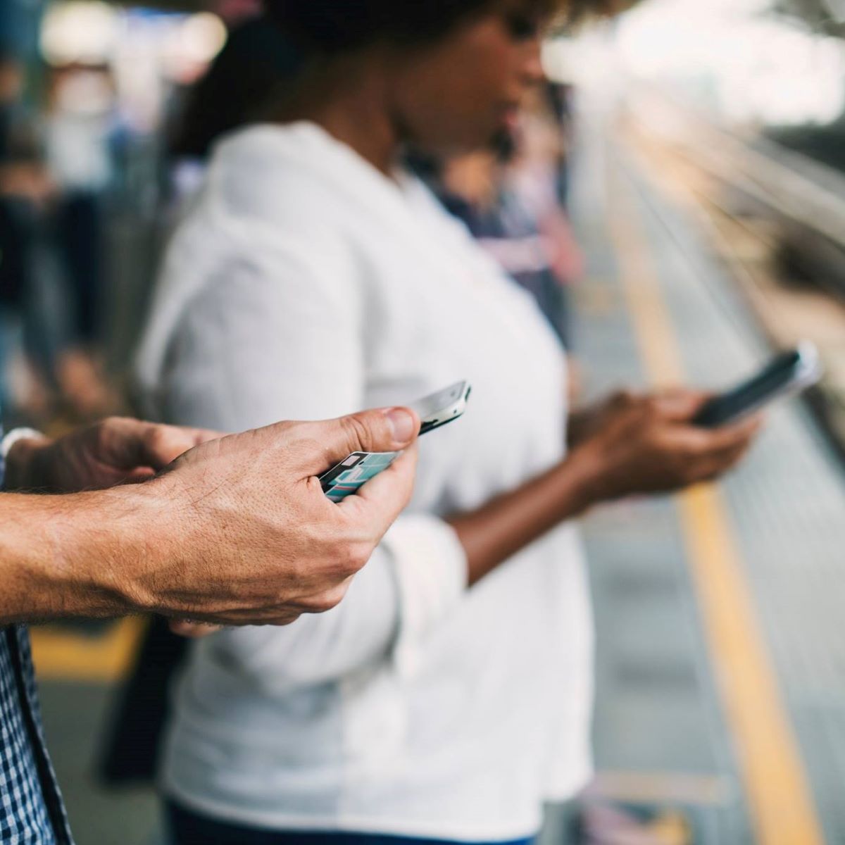Two people look at the Single Stop app on their smartphones while waiting for a train.